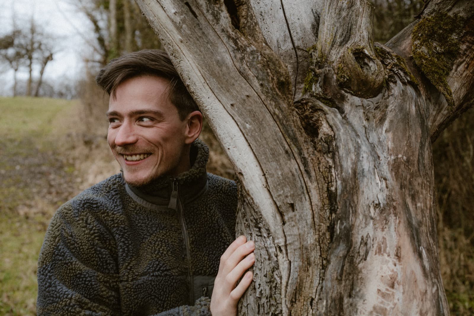 Samuel Schäck lächelnd neben einem alten Totholzstamm im Wald