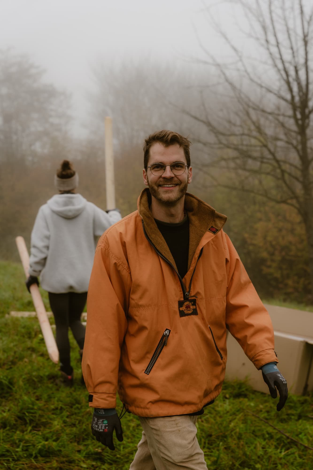 Das PermaWaldGarten-Team trägt Pfähle über ein nebliges Feld